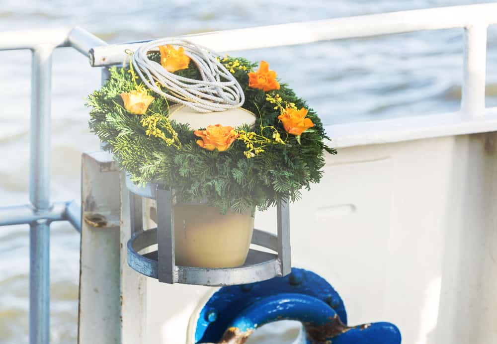 Urn with rope and orange flowers rests on a green wreath by the water for Long Island sea burials.