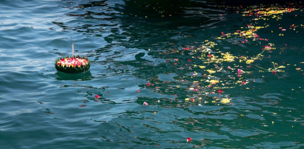 A floating floral arrangement and scattered petals drift on blue-green water for a sea burial in Long Island.